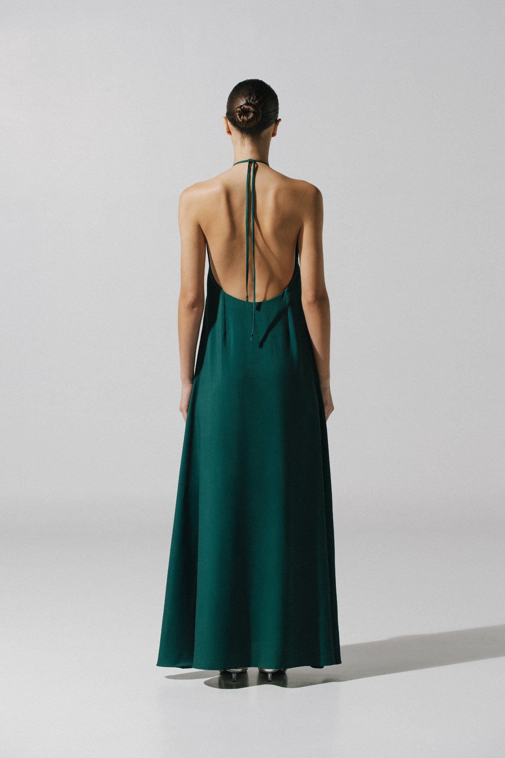 Vestido Rondine verde esmeralda en exterior urbano, escote halter y caída sofisticada.