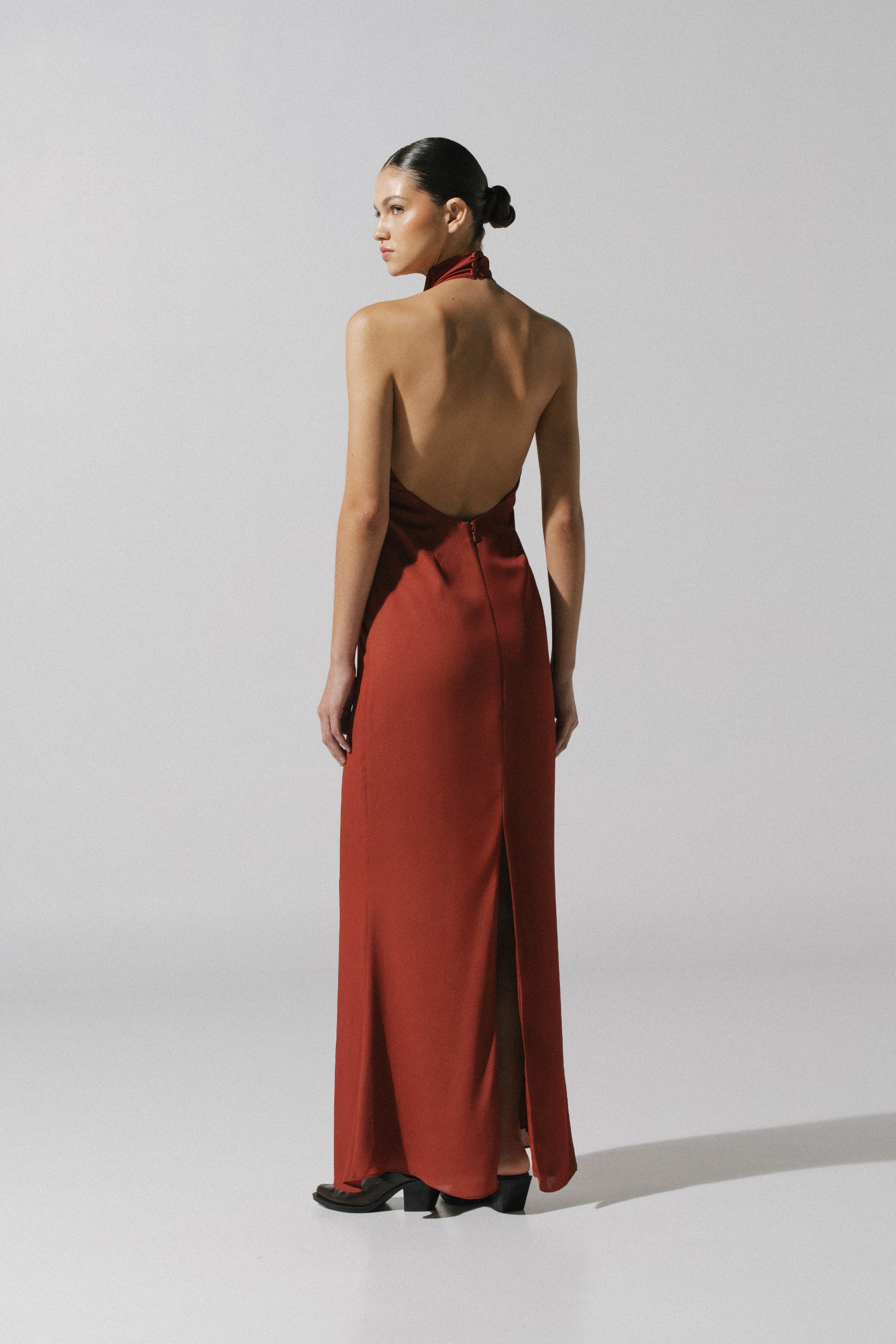 Vestido terracota Consu con corte drapeado, escote halter y silueta elegante.